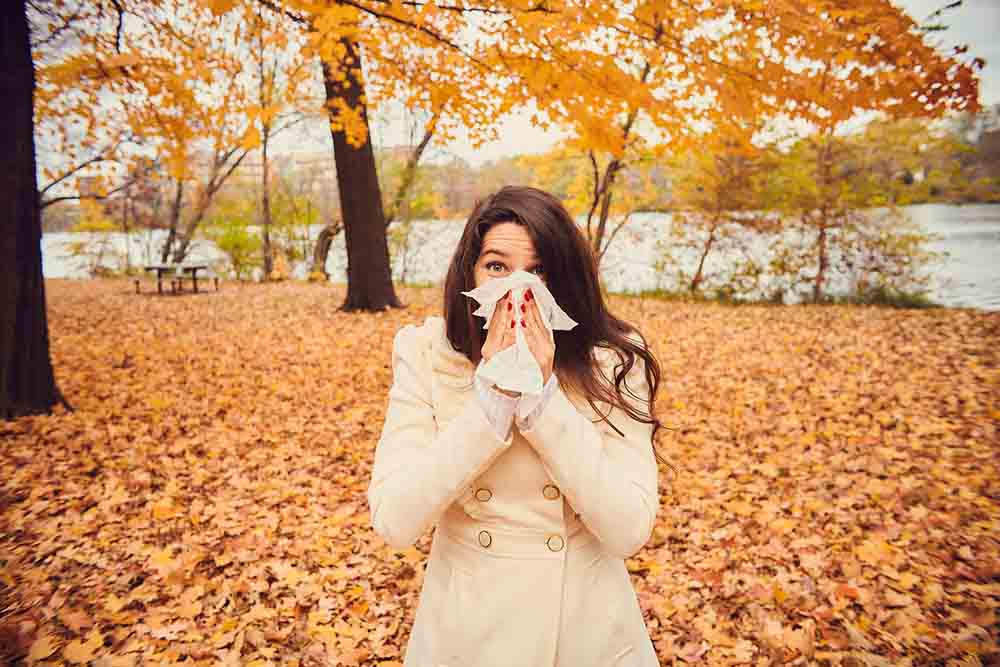 Mujer en paisaje otoñal estornudando